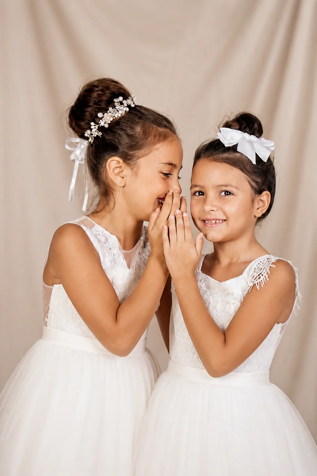 Two flower girls in white dresses sharing a secret