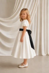 Side view of the Poppy ivory flower girl dress by TH&TH showing the black satin sash tied in a bow at the waist