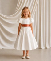Poppy ivory matte satin flower girl dress by TH&TH with a removable terracotta satin sash tied in a bow, front view